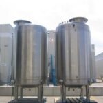 Two vertical stainless steel storage tanks at industrial facility