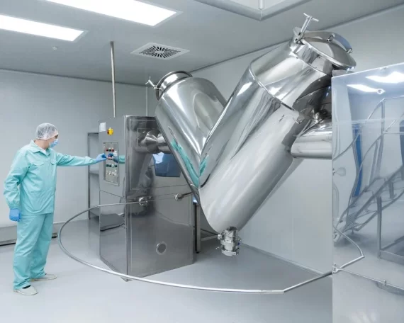 Pharmaceutical cleanroom technician operating stainless steel mixing equipment.