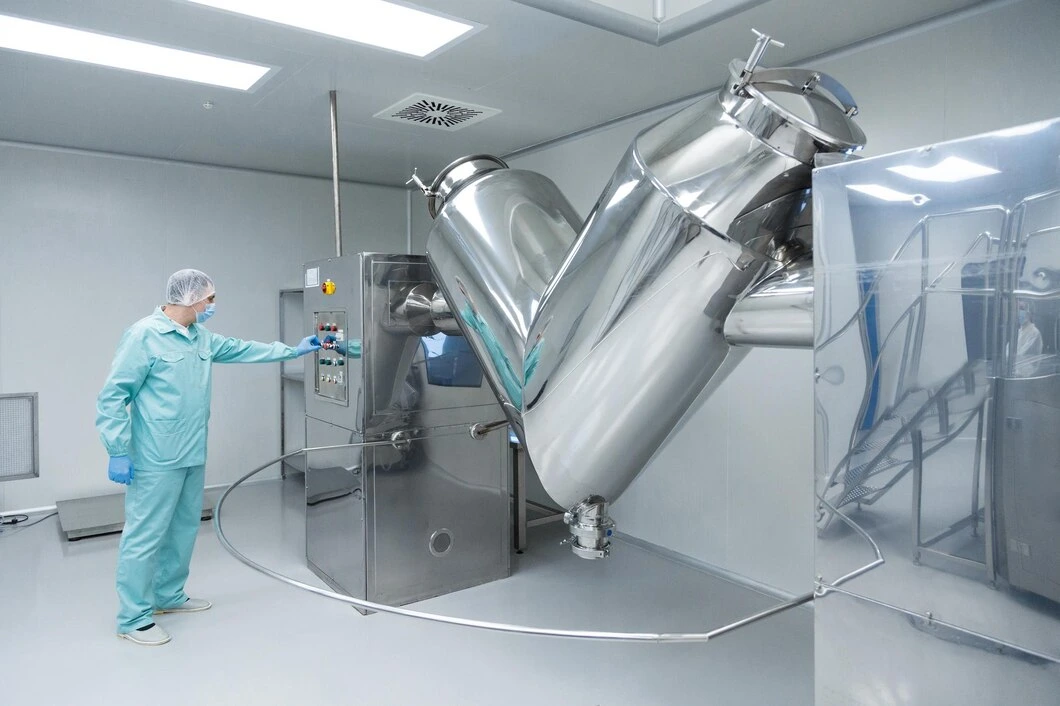 Pharmaceutical cleanroom technician operating stainless steel mixing equipment.